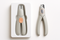 LED pet nail clippers with paw design packaged and unpackaged on a white tray